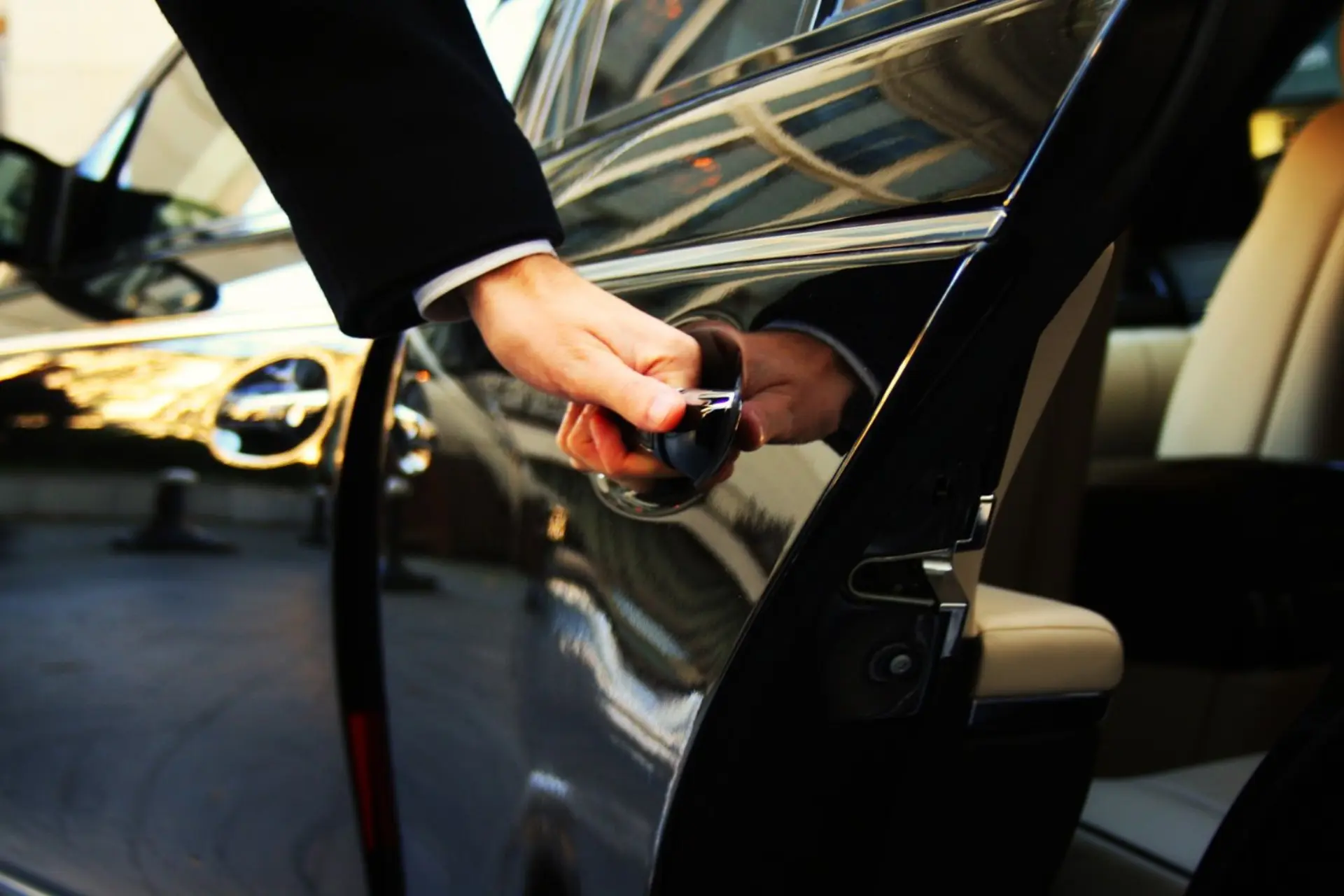 A professional chauffeur opening the rear door of a black luxury SUV at a terminal curb — Luxe Elite Transportation flight-tracked LAX, SNA, LGB and BUR airport transfers with Luxe Elite Transportation